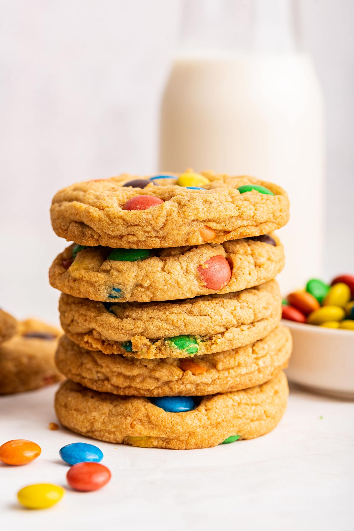 stack of M&M cookies in front of a glass of milk.