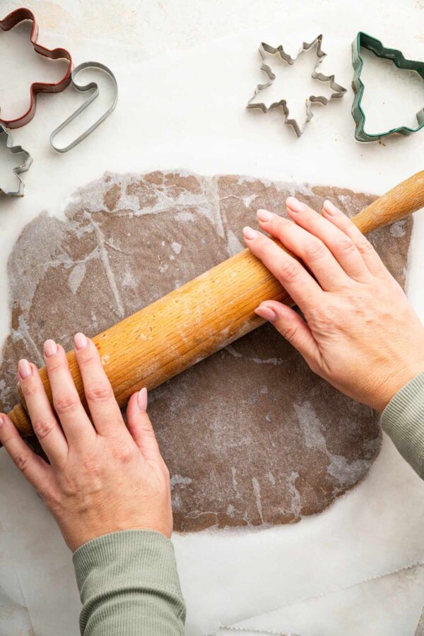 rolling out gingerbread dough between two pieces of parchment paper.