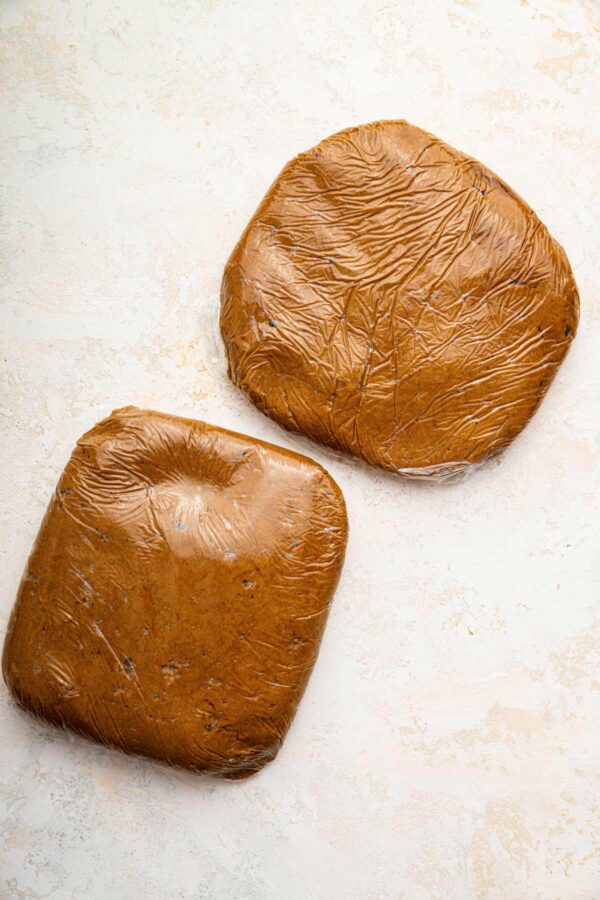 two flattened discs of gingerbread dough wrapped in plastic wrap.