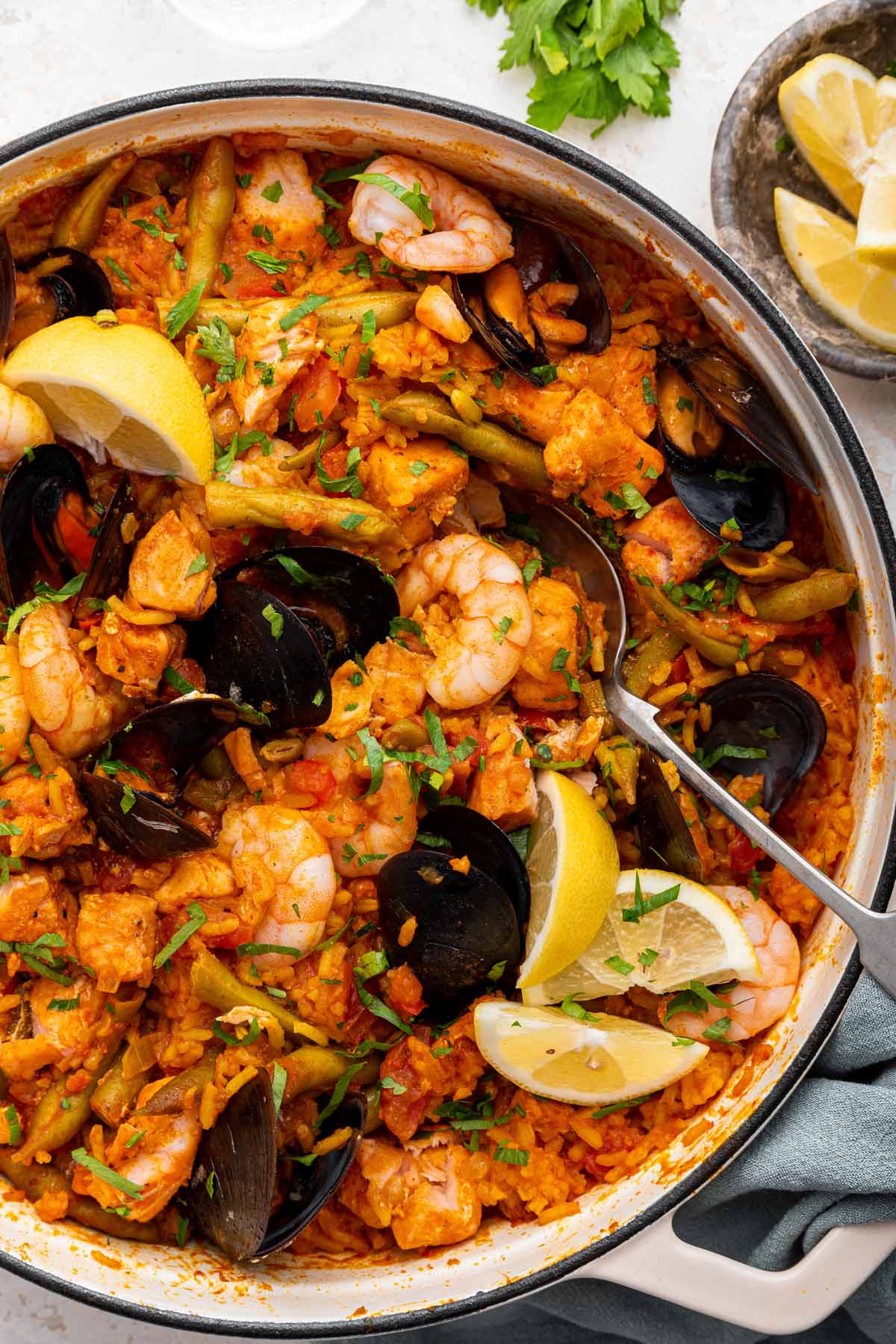 spoon scooping out shrimp from a large pot of salmon paella.
