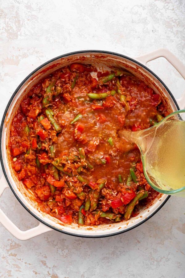 pouring stock into homemade paella.