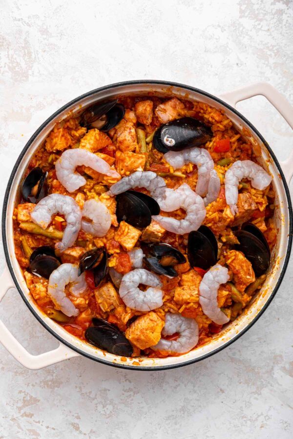 mussels and shrimp added to a pan of paella.