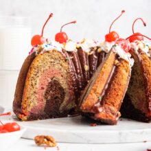 chocolate and strawberry swirled banana split bundt cake with whipped cream and cherries on top.