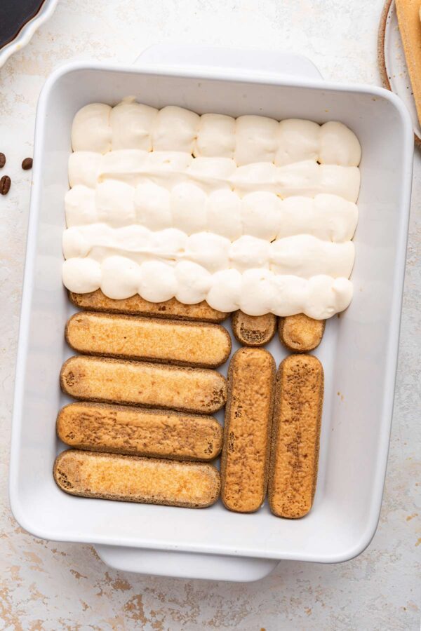 covering a layer of soaked ladyfingers with mascarpone cream.