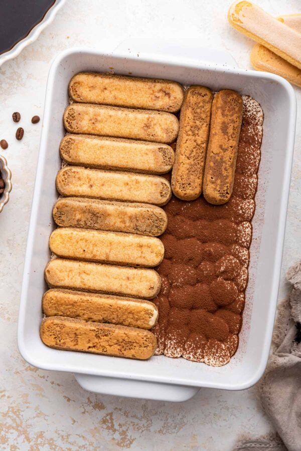 placing a second layer of ladyfingers over a dish of tiramisu.
