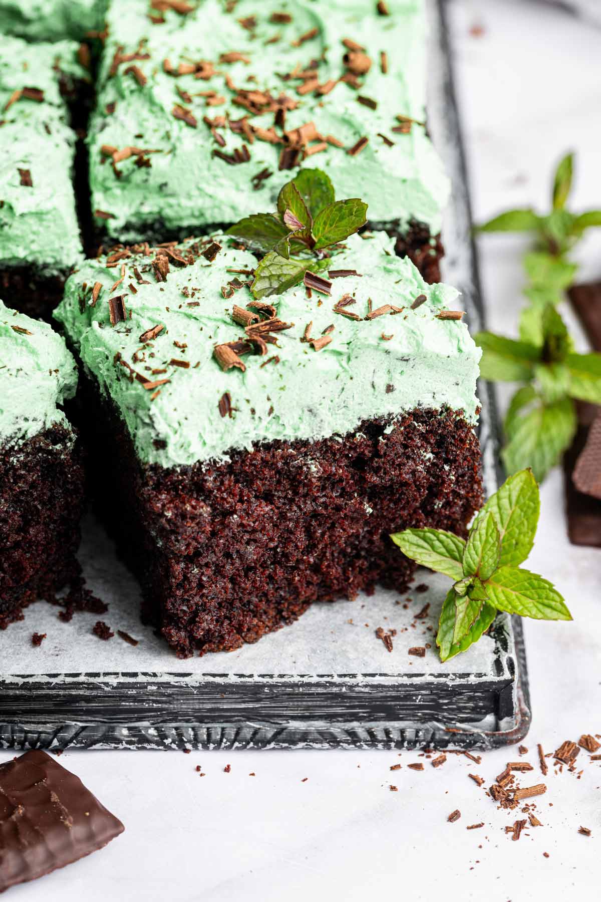 slice of chocolate cake with mint chip frosting next to fresh mint.
