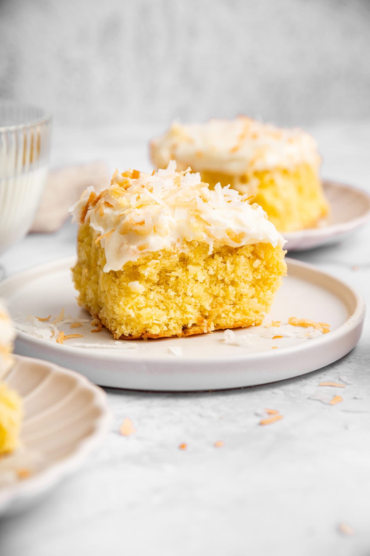 two slices of coconut sheet cake on decorative dessert plates.
