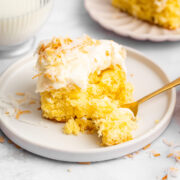 a slice of coconut sheet cake on a dessert plate with one forkful removed.