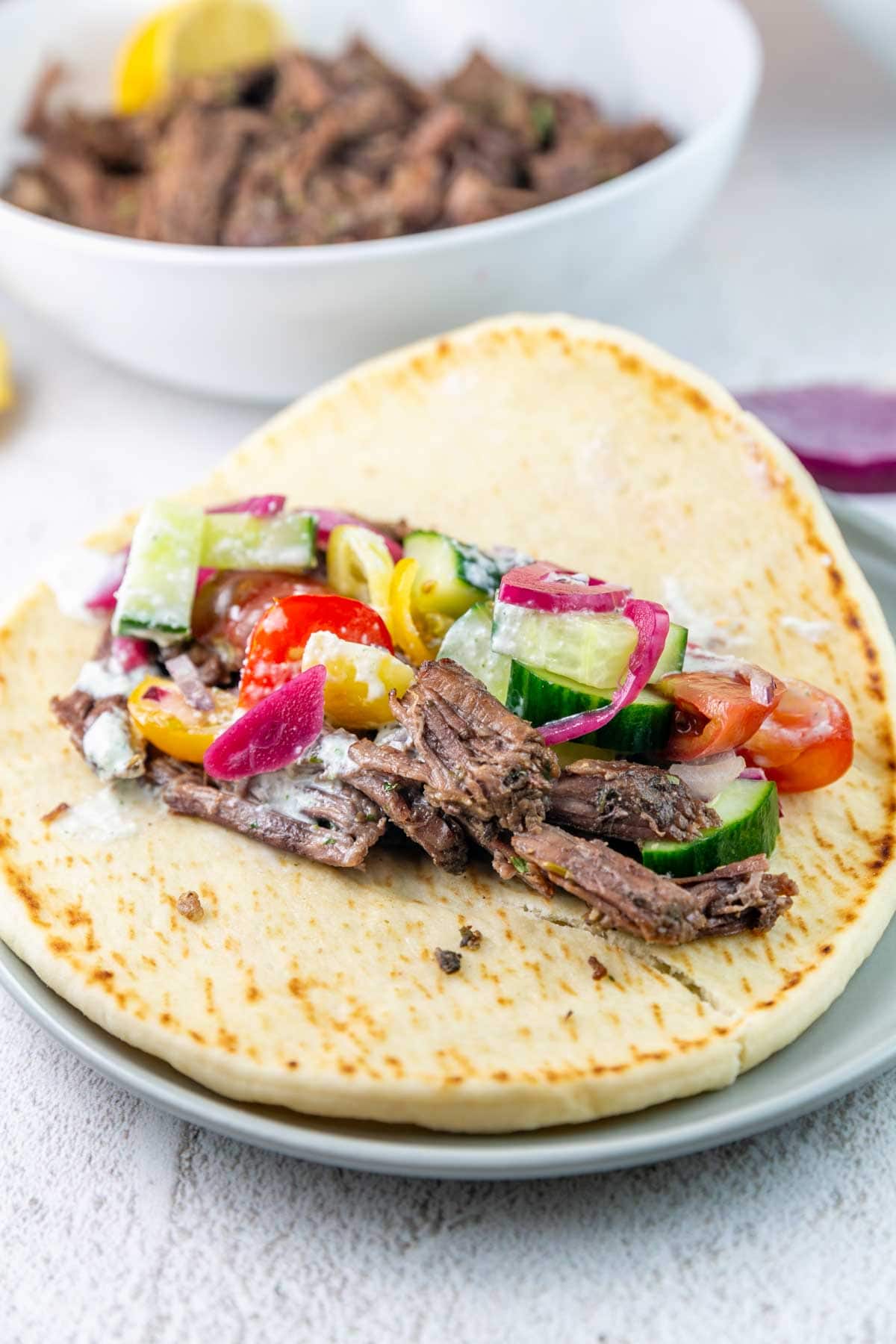 large pita bread with shredded beef, tomatoes, cucumbers, and tzatziki.