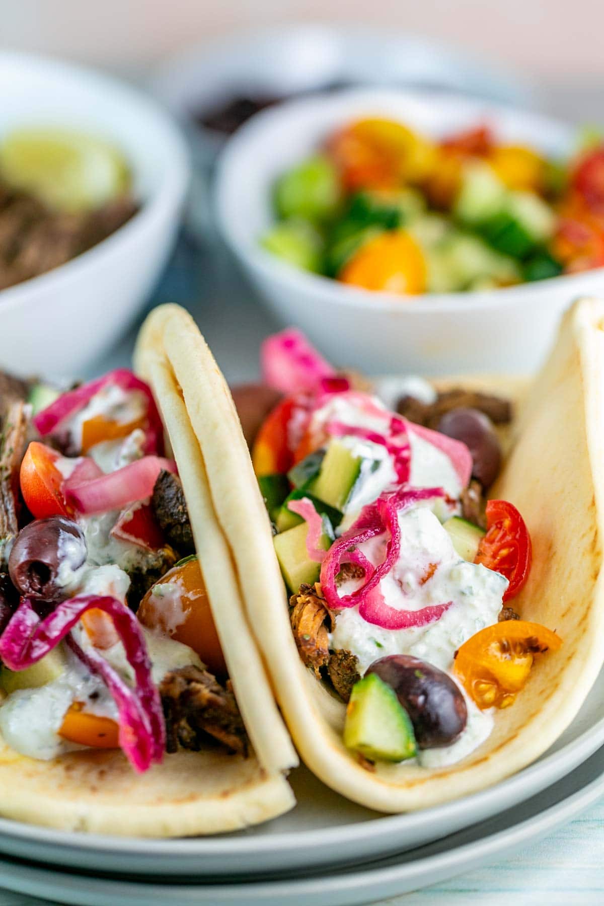 two pitas filled with shredded beef, tomatoes, cucumbers, olives, red onions, and tzatziki sauce.