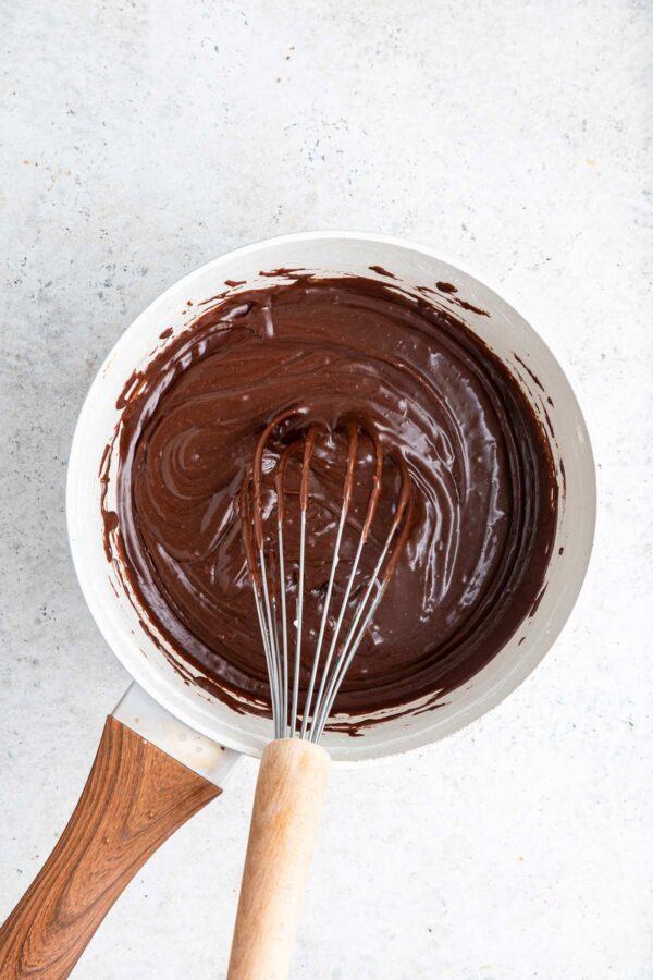 whisking together hot fudge frosting for a cake.