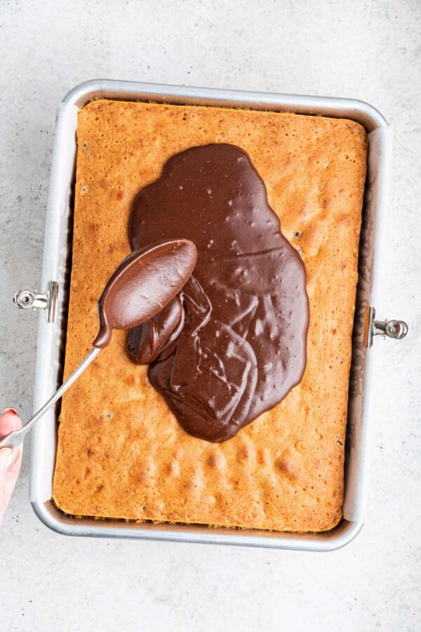 pouring warm hot fudge frosting over a chocolate chip sheet cake.