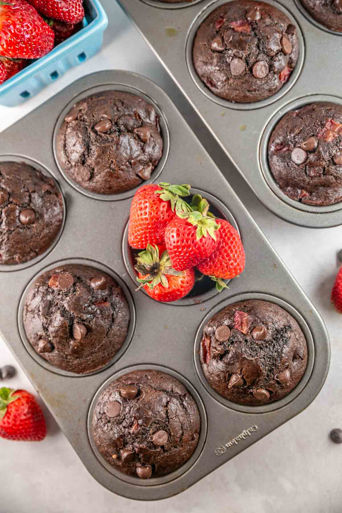 chocolate strawberry muffins in a muffin tin with a big pile of strawberries.