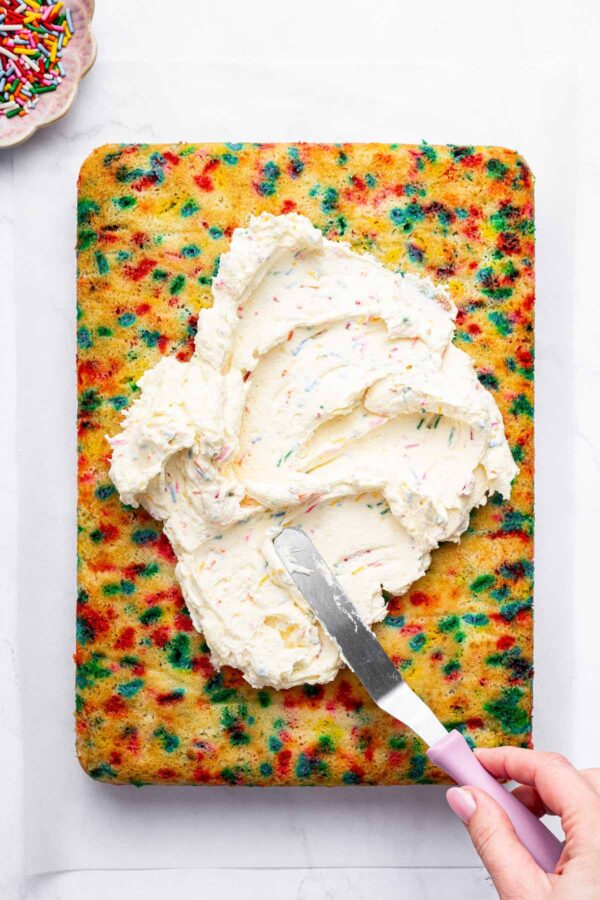 spreading frosting on a funfetti sheet cake.