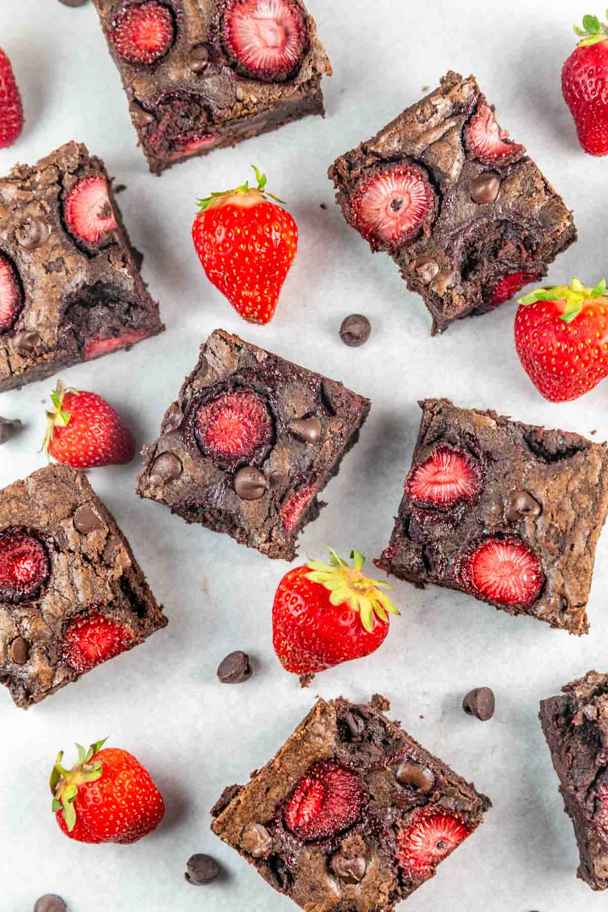 squares of fudgy strawberry brownies surrounded by chocolate chips and strawberries.