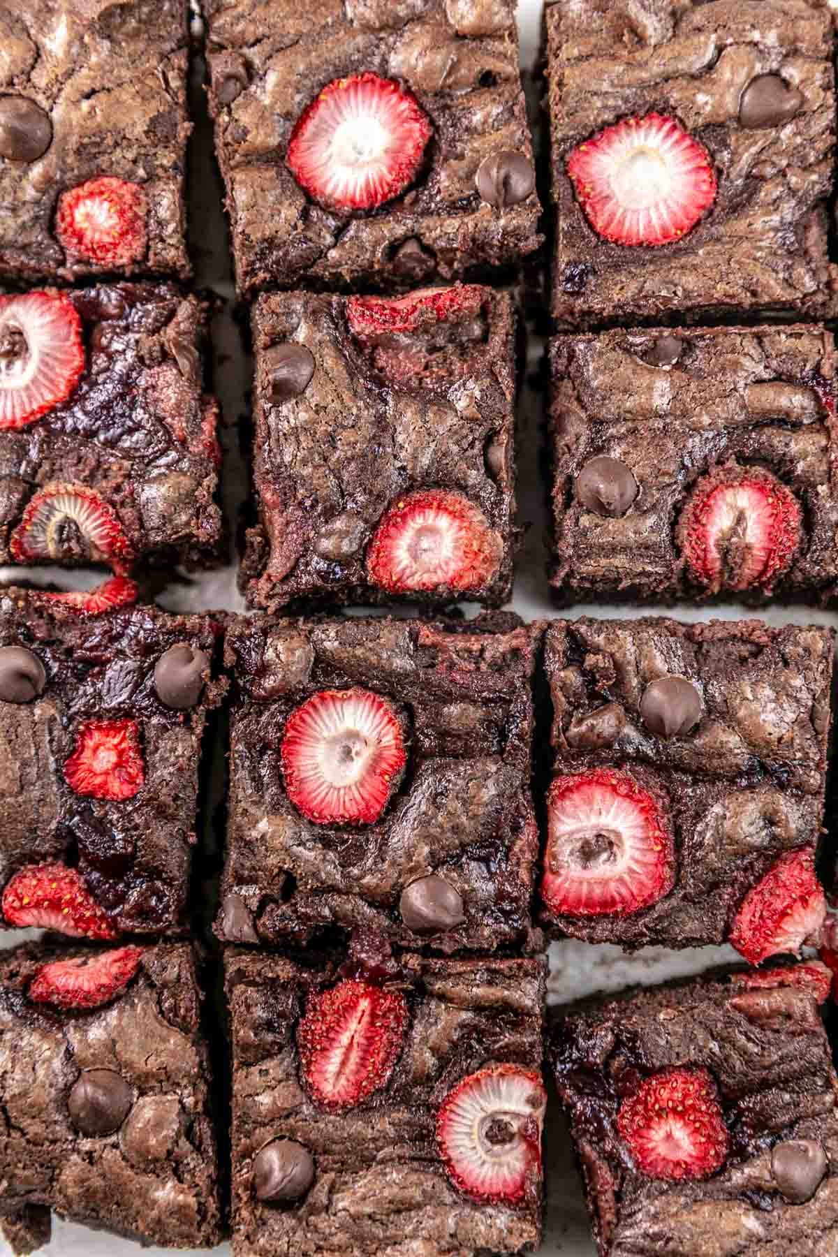 fudgy brownies cut into squares and topped with roasted strawberries and chocolate chips.