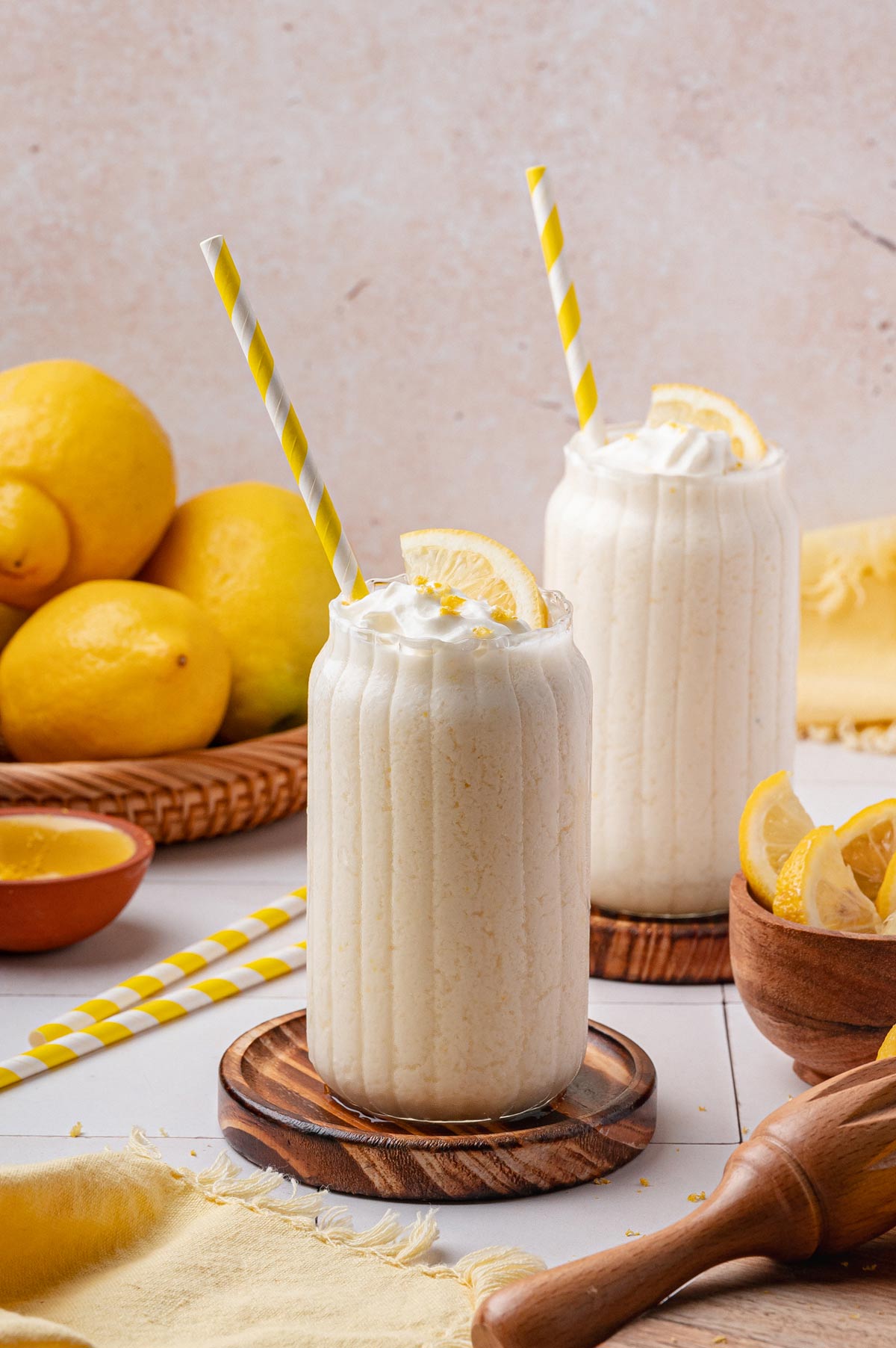 two glasses of creamy frozen lemonade on wooden coasters.