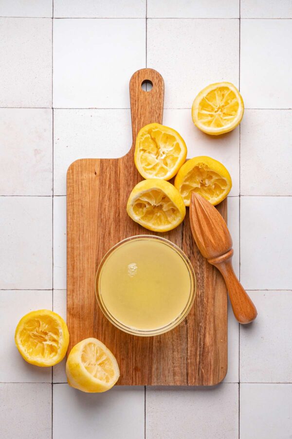 a bowl of freshly squeezed lemon juice next to the squeezed lemons.