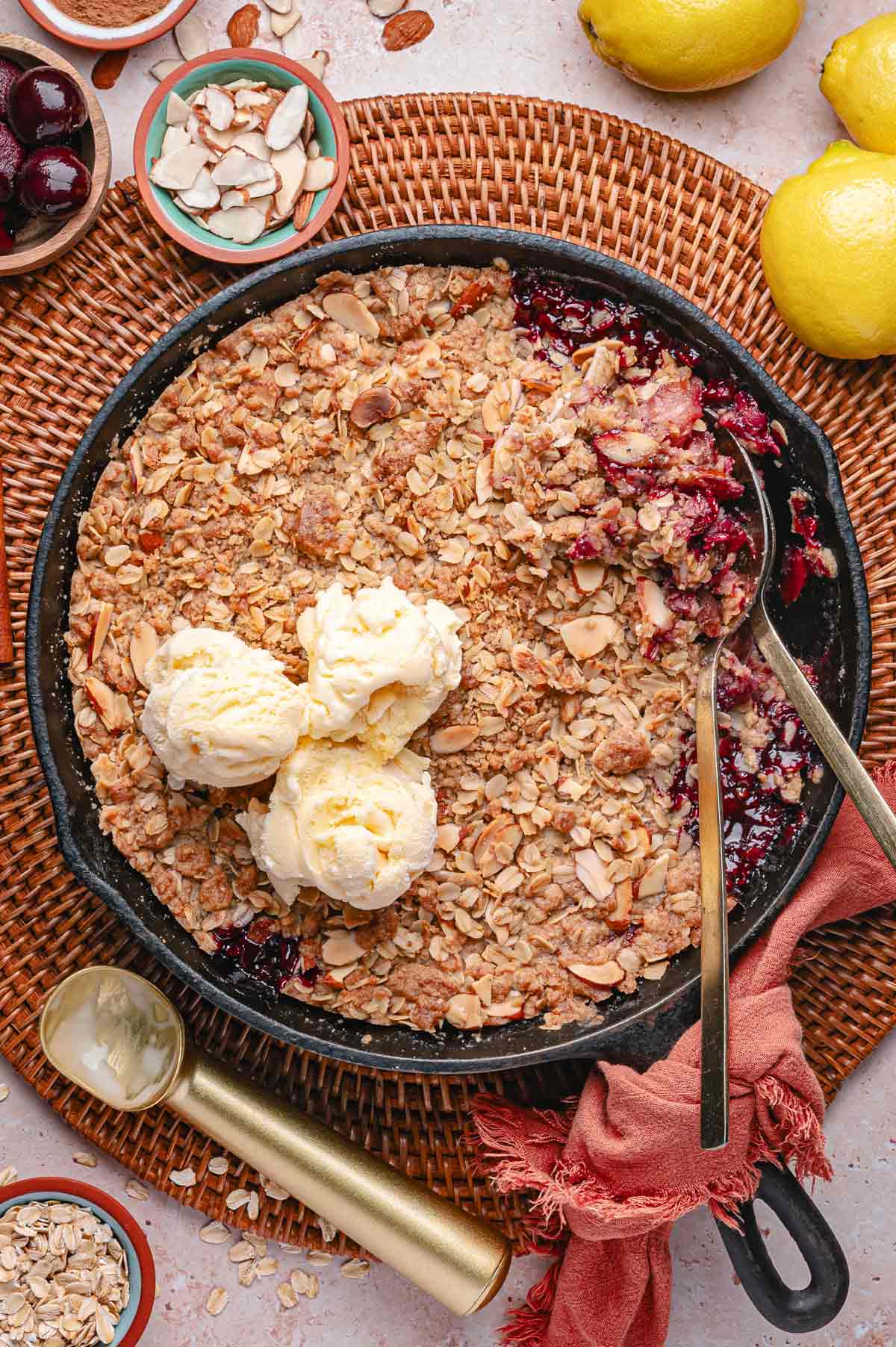 peach cherry crisp in a cast iron skillet topped with scoops of ice cream.