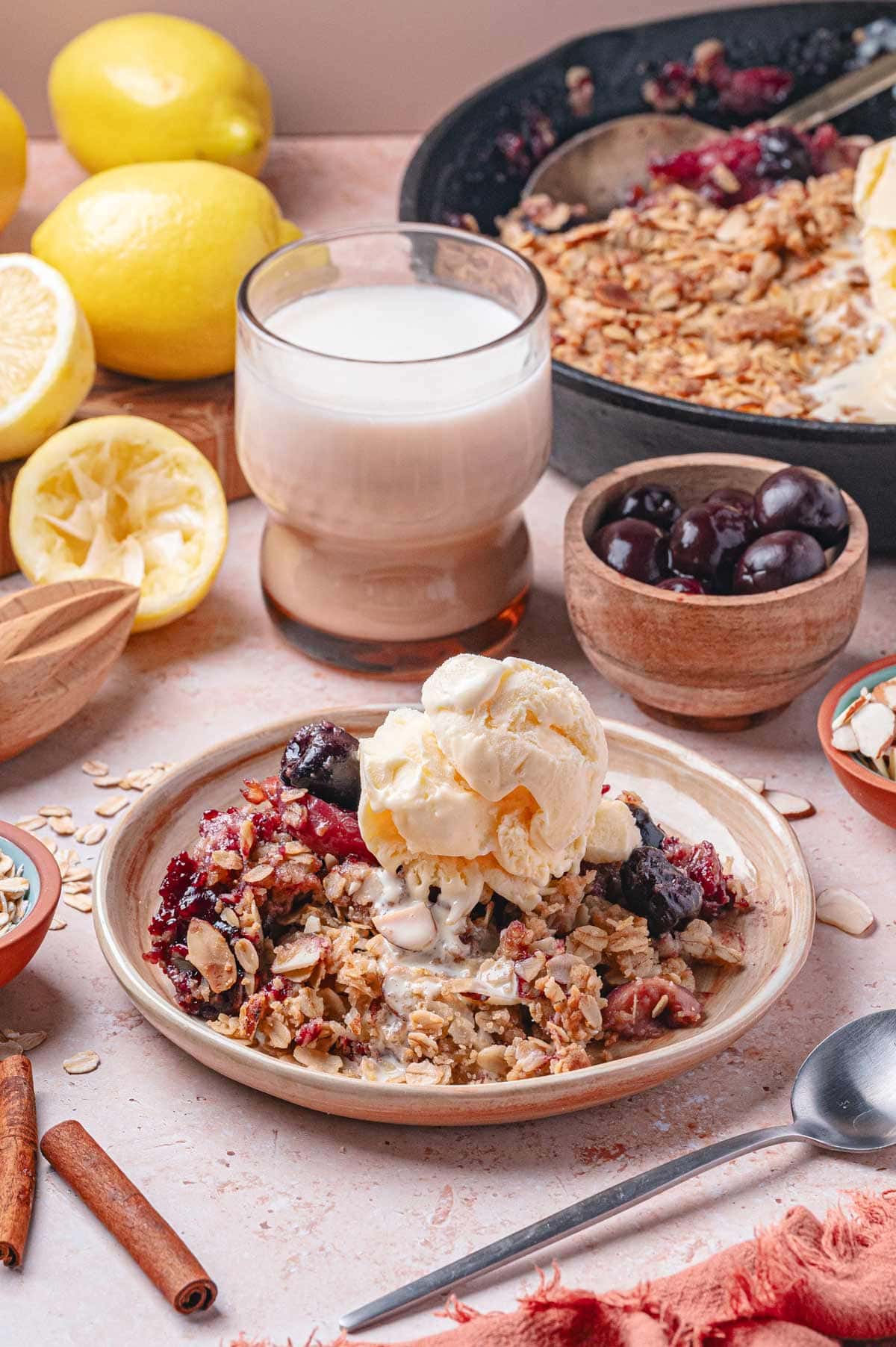 serving of peach cherry crisp on a plate topped with vanilla ice cream.