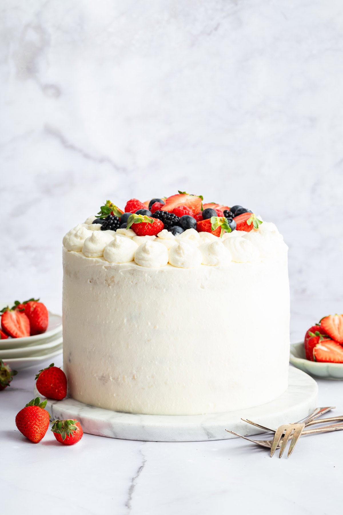 three layer berry cake covered in chantilly frosting with a pile of fresh berries on top.
