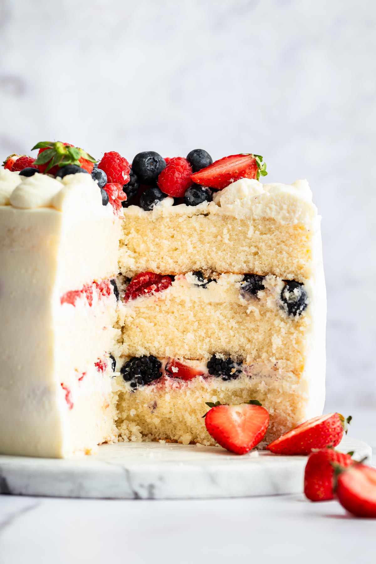 three layer white cake cut open to show the thick layer of frosting and berries.