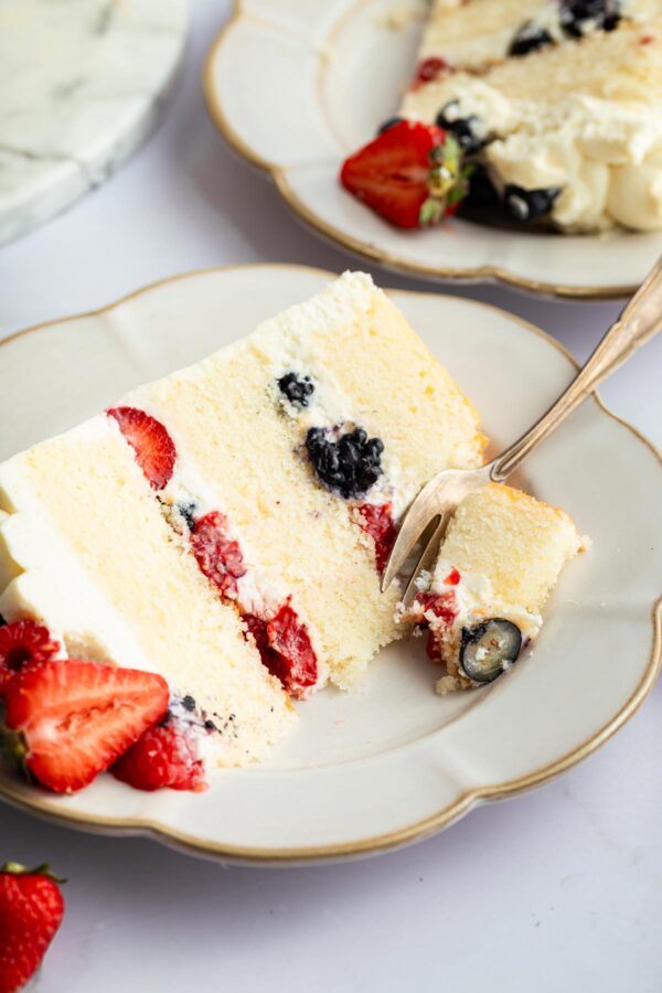 close up view of a slice of berry chantilly cake with one forkful removed.
