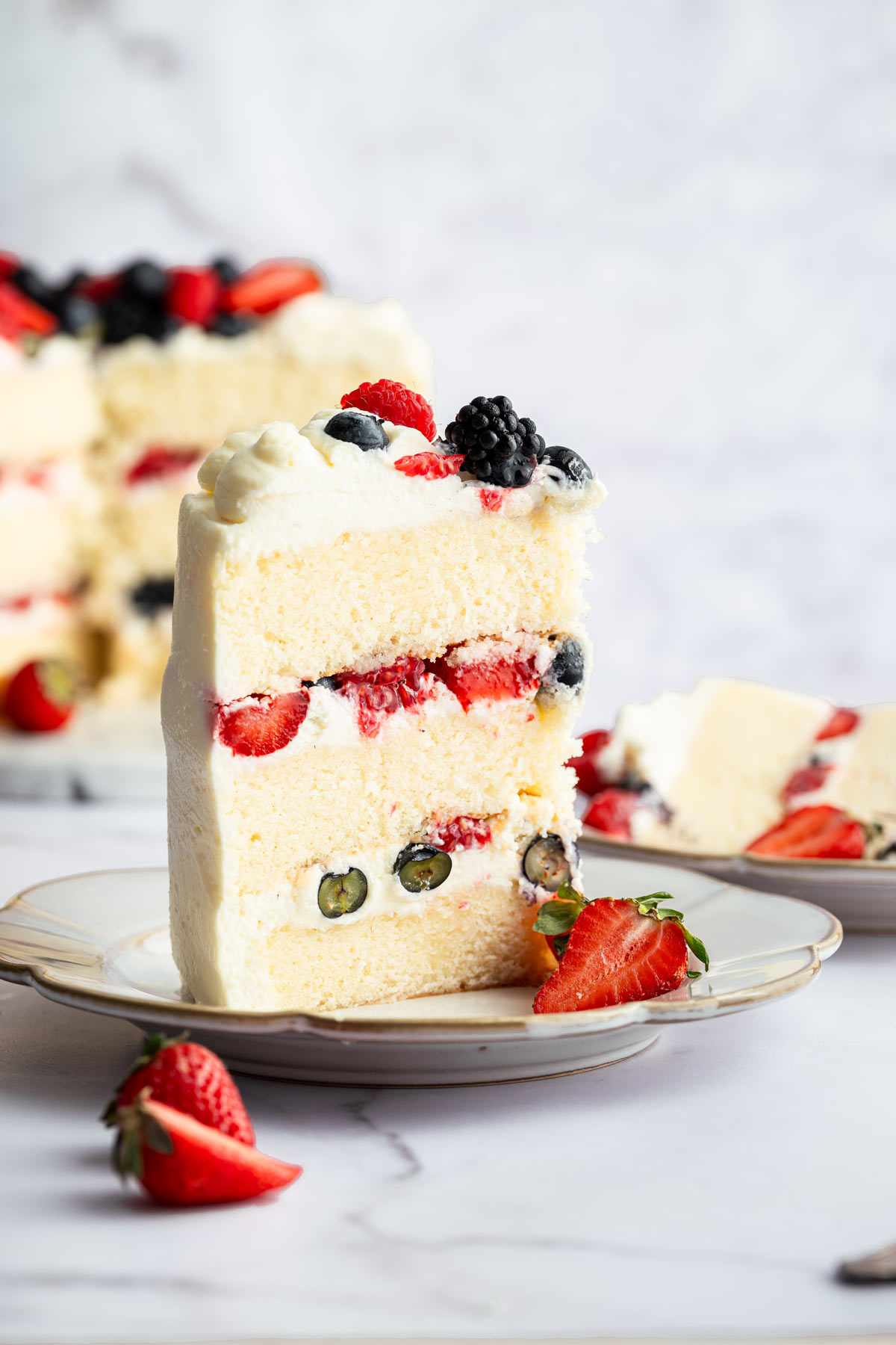 slice of berry chantilly cake standing upright on a dessert plate.