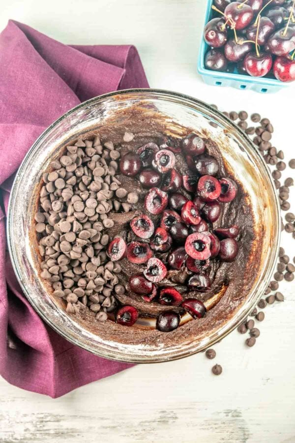 adding chocolate chips and halved cherries to brownies.