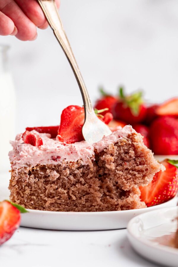 a fork digging into a slice of strawberry sheet cake.