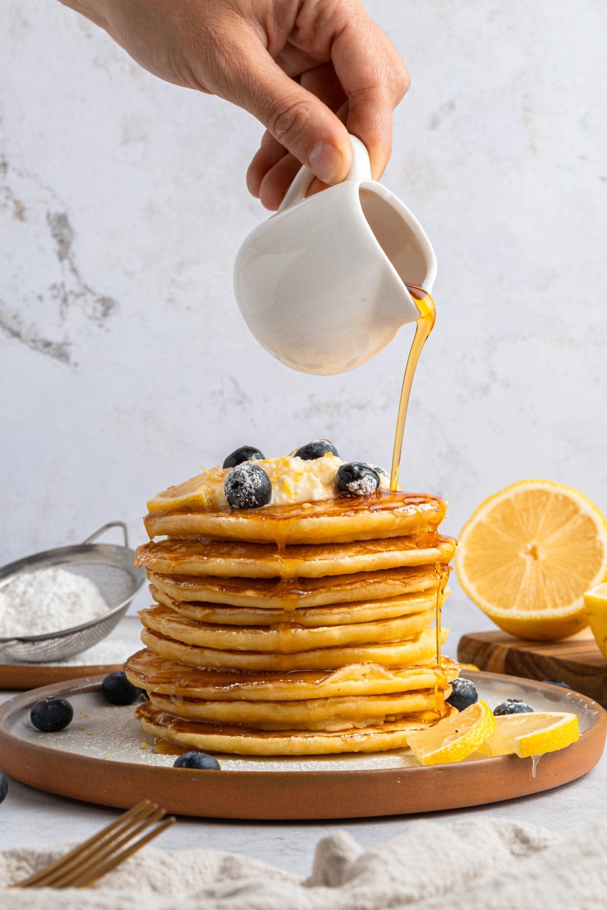 pouring maple syrup on a tall stack of pancakes.