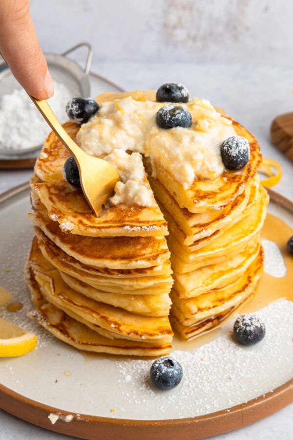 fork digging into a stack of lemon ricotta pancakes.
