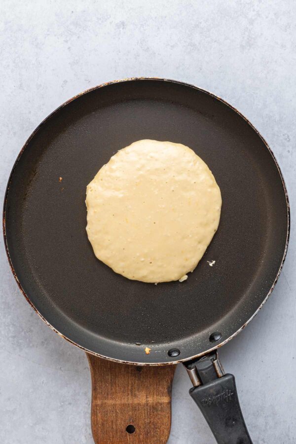 cooking a pancake in a skillet until bubbles form on the surface.