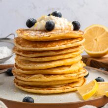 tall stack of lemon ricotta pancakes with whipped ricotta and blueberries.