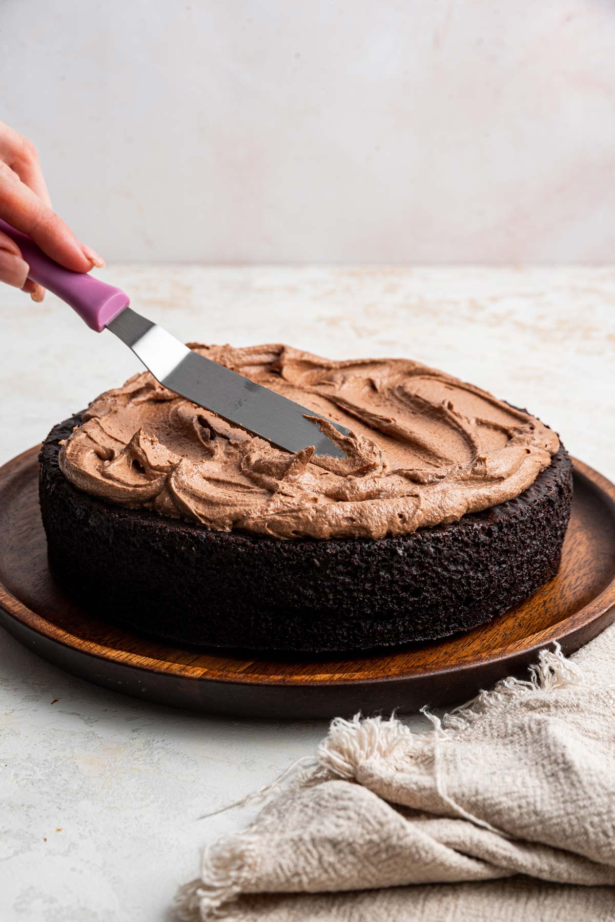 fluffy chocolate buttermilk frosting being spread on a dark chocolate cake.