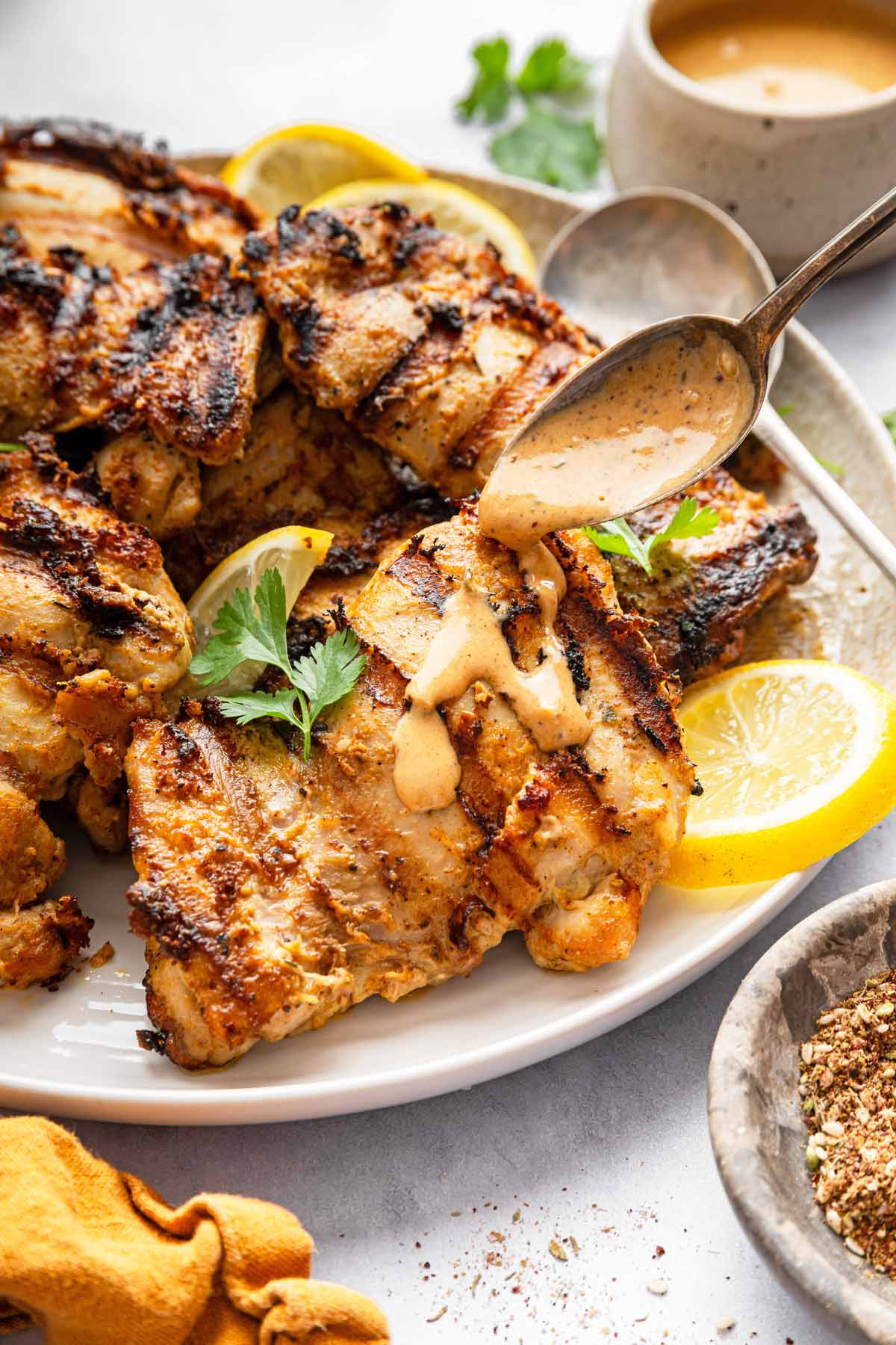 spooning tahini sauce on grilled chicken.