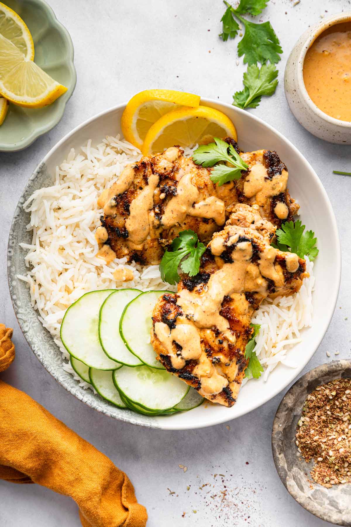 grilled tahini chicken in a bowl with rice and sliced cucumbers. 
