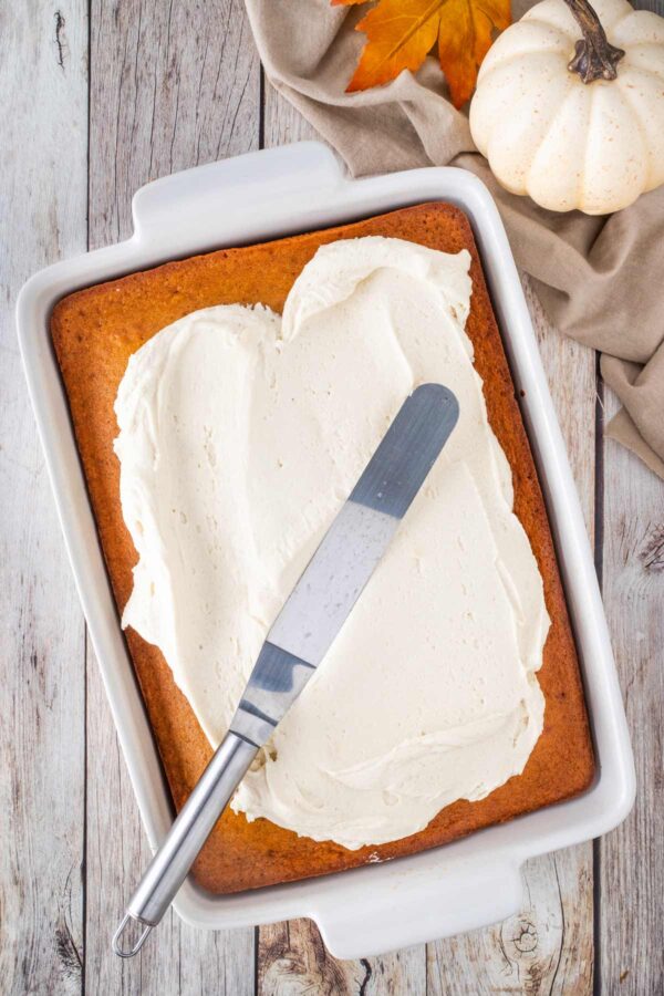 spreading maple cream cheese frosting on a pumpkin cake.