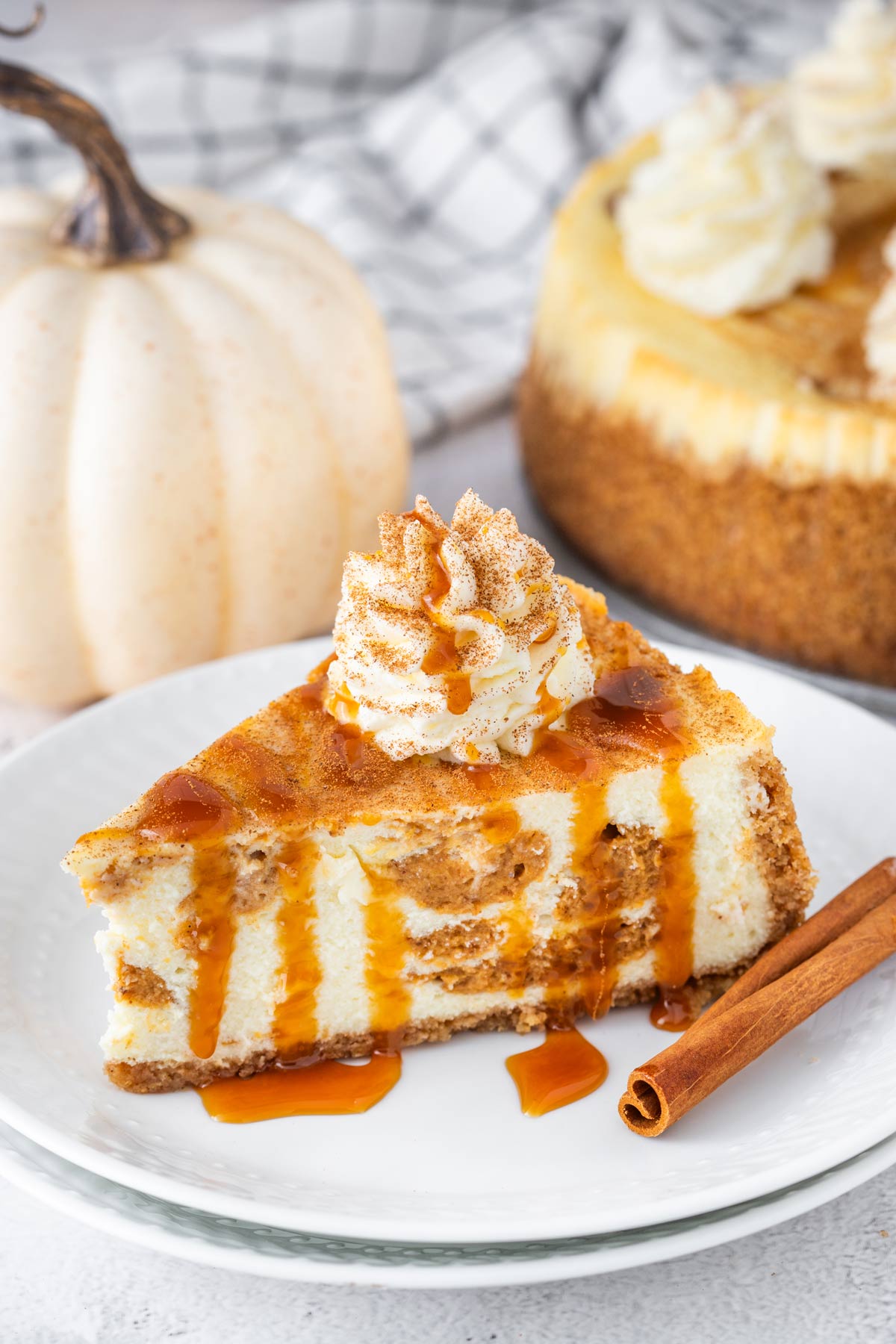 slice of pumpkin swirl cheesecake drizzled with caramel sauce and cinnamon whipped cream.
