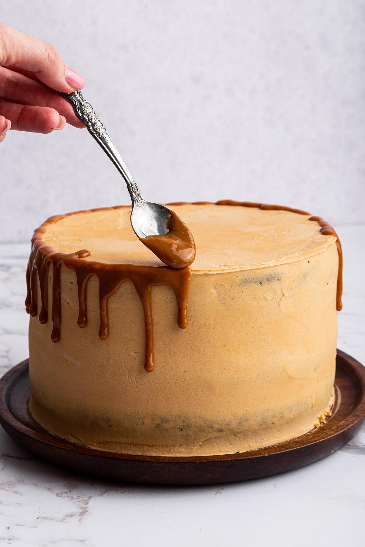 spooning caramel sauce on a cake with caramel buttercream frosting.