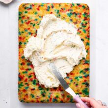 spreading a pile of homemade funfetti buttercream on a sheet cake.