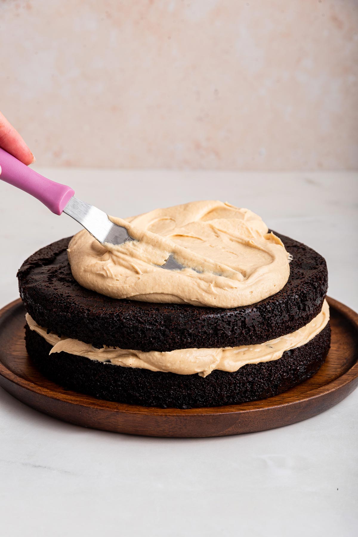 spreading a thick layer of peanut butter frosting on a chocolate cake.