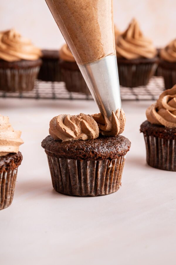 piping chocolate frosting onto a cupcake.