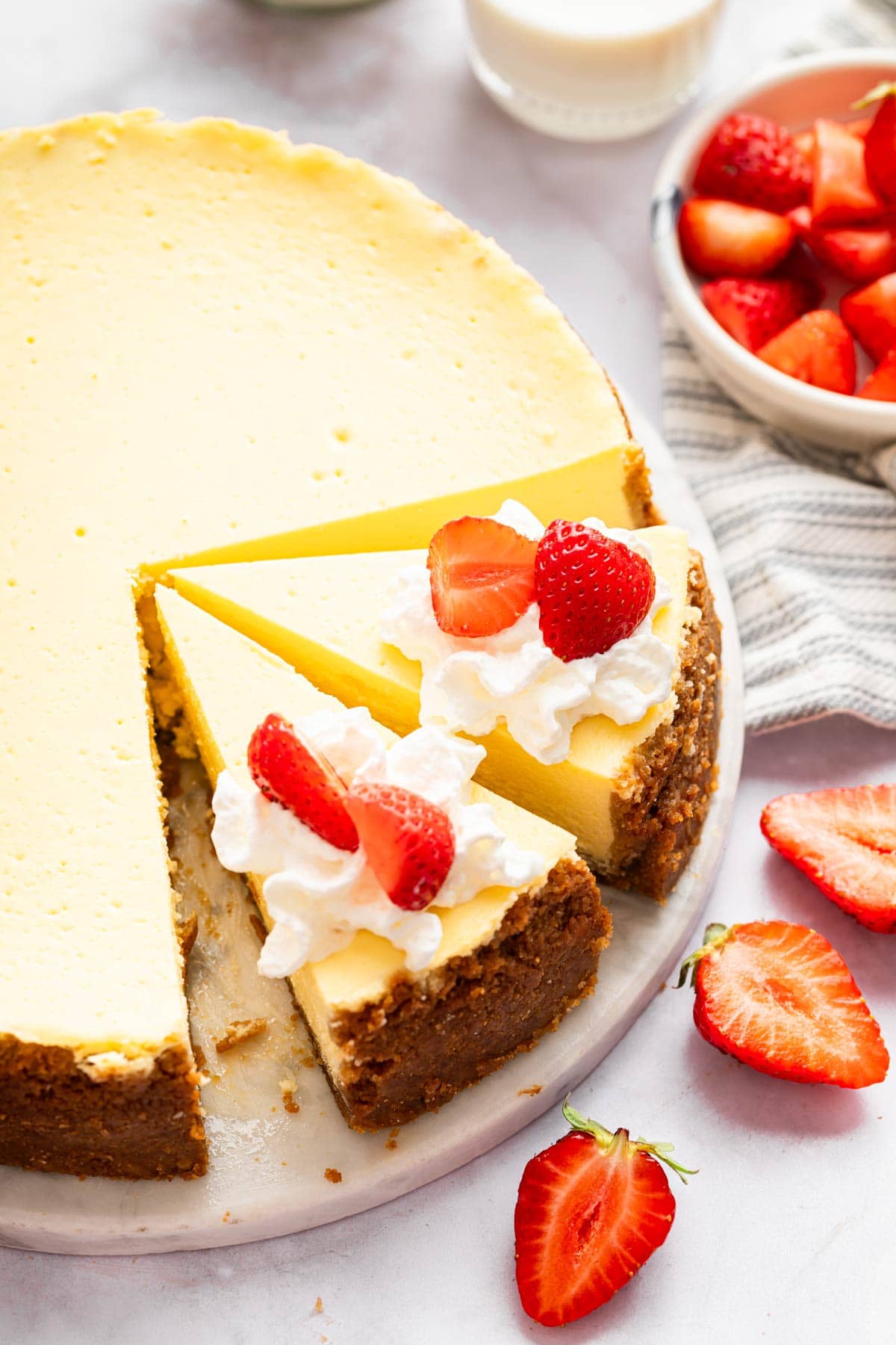 New York style cheesecake with two slices cut and topped with strawberries.