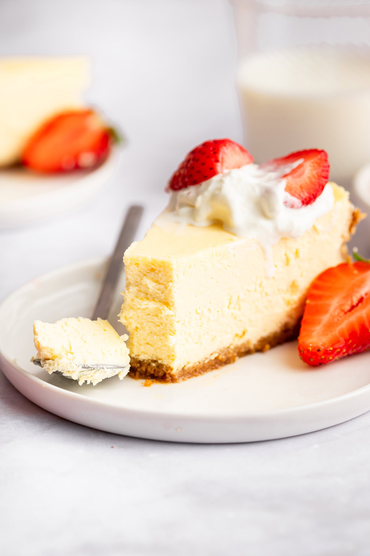 slice of cheesecake topped with strawberries with one forkful removed.