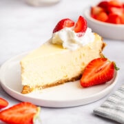 slice of creamy cheesecake topped with whipped cream and strawberries.