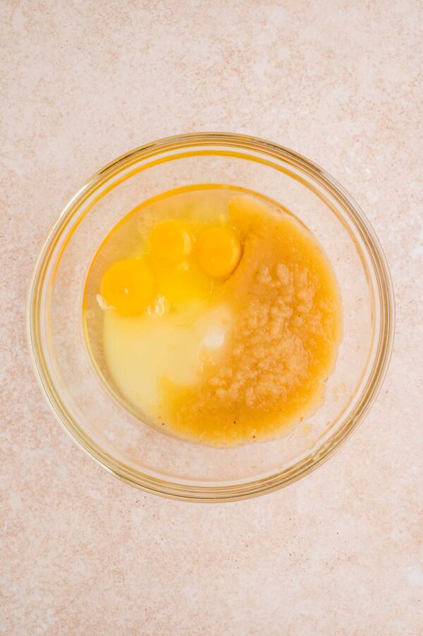 eggs, sugar, oil, and applesauce in a glass mixing bowl.