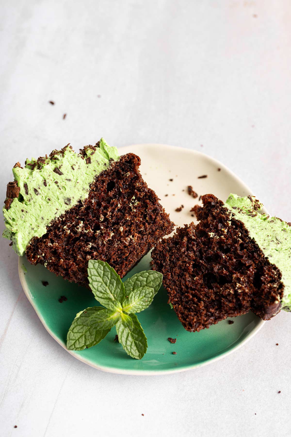 chocolate cupcake with mint chip frosting cut in half showing the fluffy cupcake interior.
