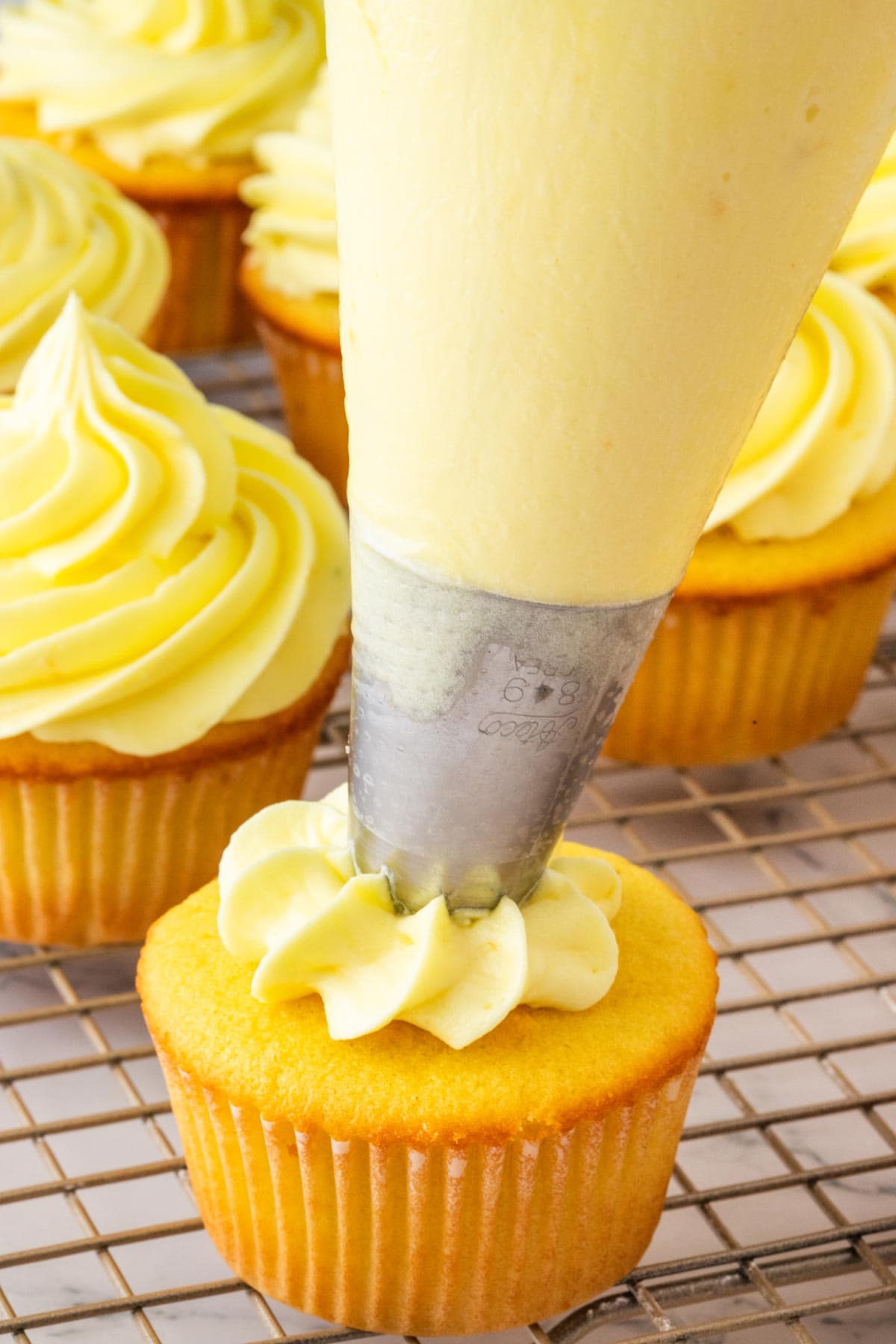 piping cream cheese frosting onto cupcakes.