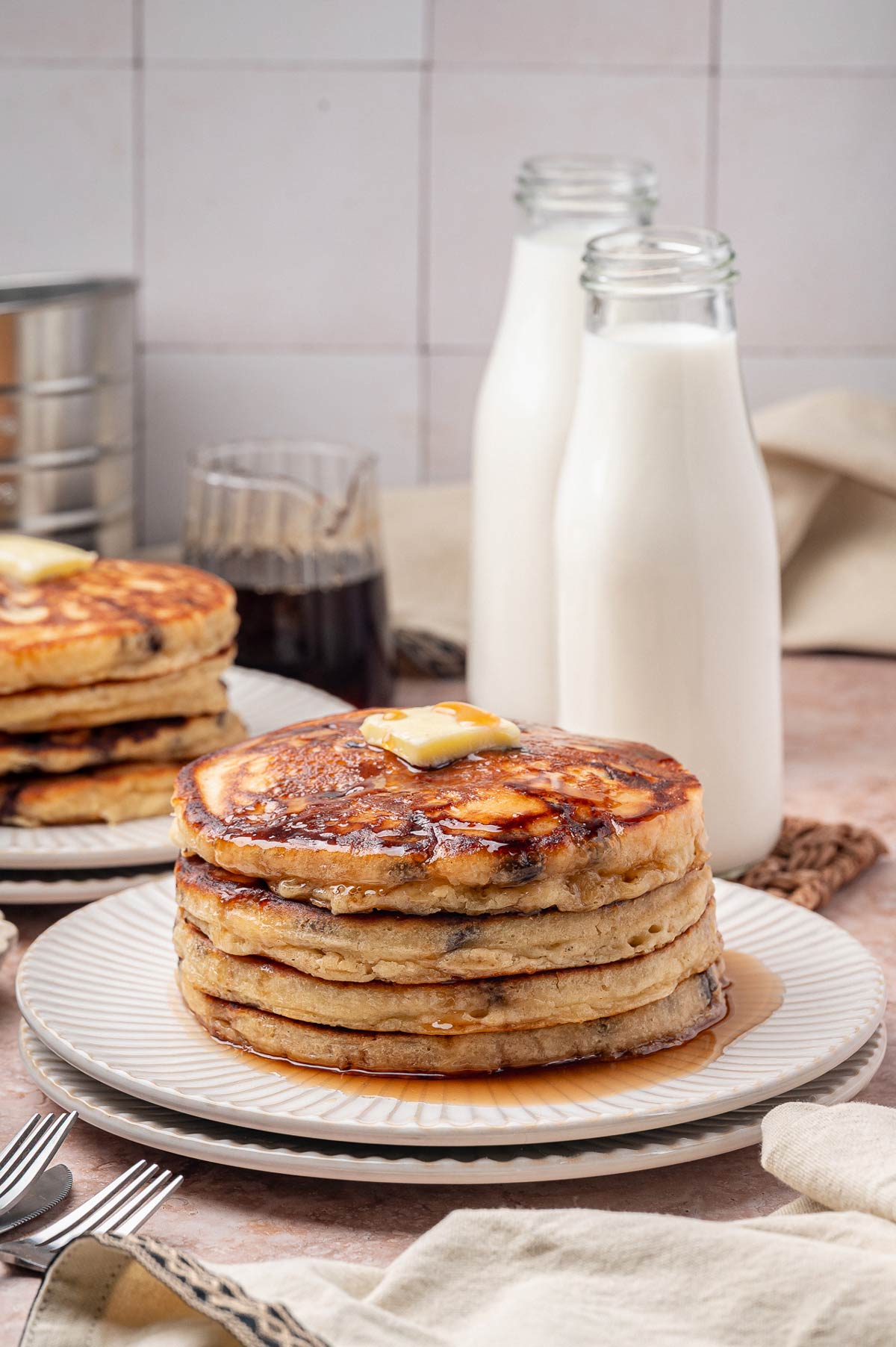 tall stack of chocolate chip pancakes covered with maple syrup and a pat of butter.